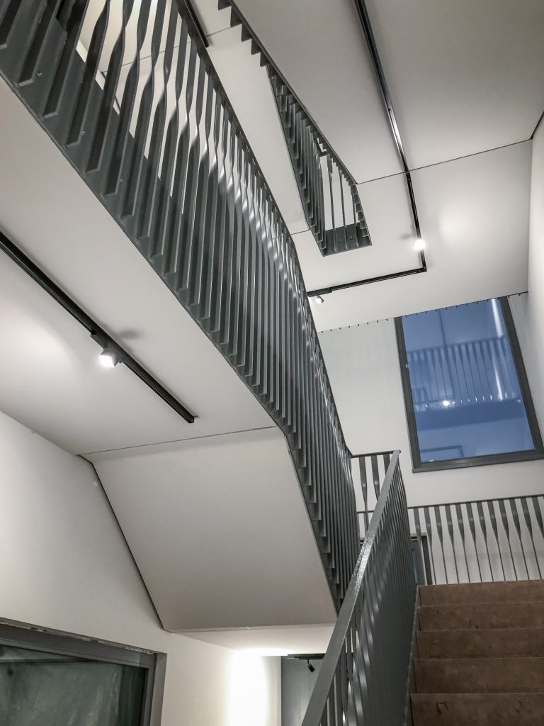 Modernisiertes Treppenhaus mit hellem Anstrich, dunklem Metallgeländer und Holzhandlauf