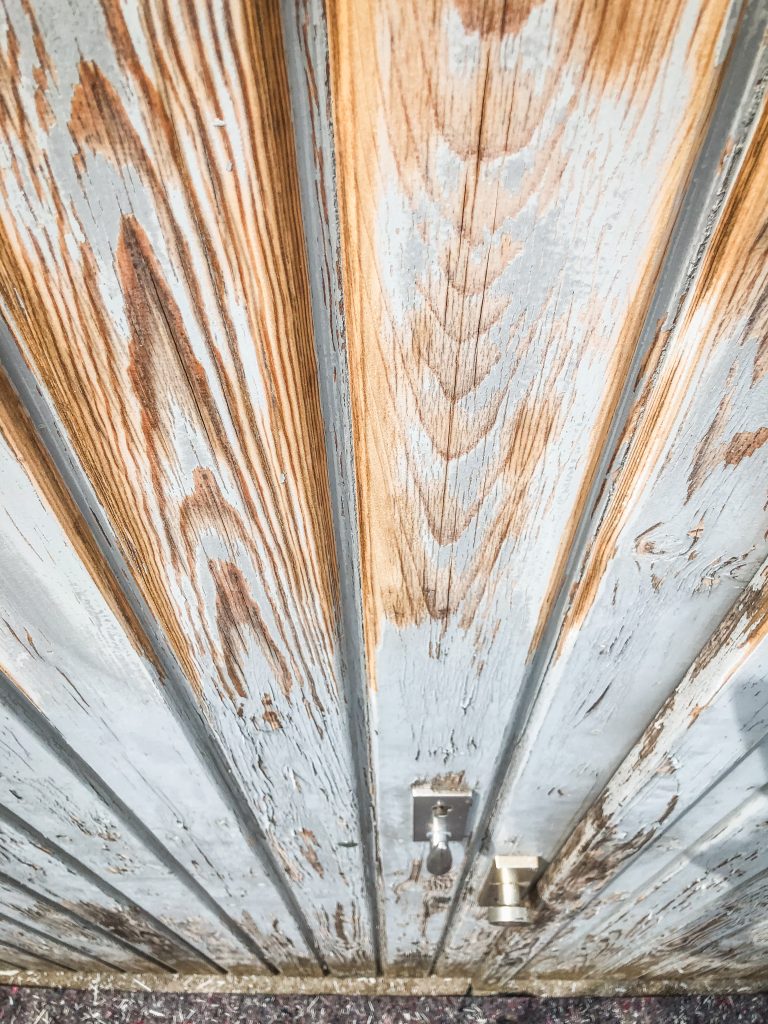 Detailaufnahme einer verwitterten Holztür mit abgeblätterter Farbe vor der Renovierung