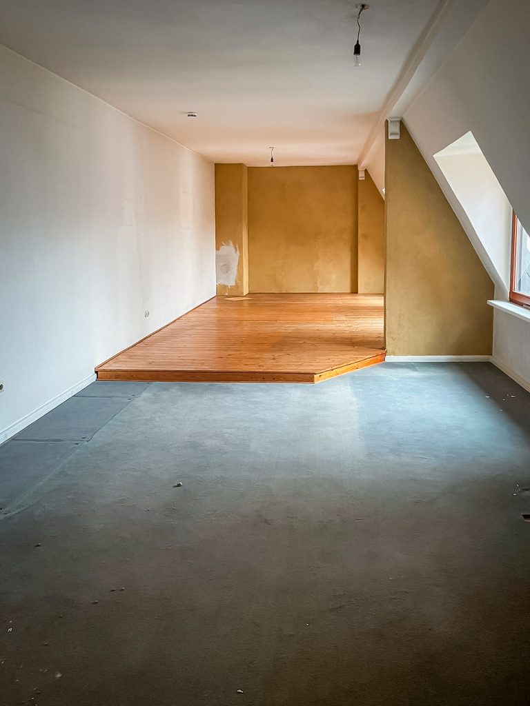 Dachgeschossraum vor der Renovierung mit Teppichboden, Holzwand und sichtbaren Gebrauchsspuren