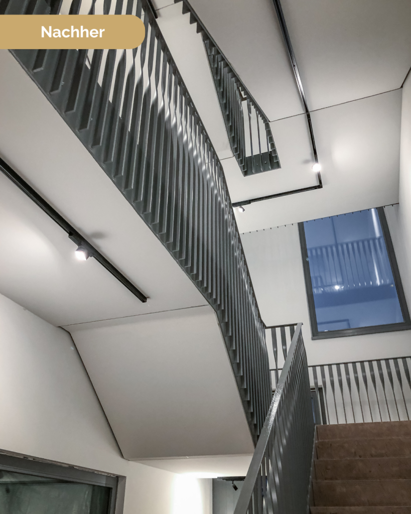 Modernisiertes Treppenhaus mit hellem Anstrich, dunklem Metallgeländer und Holzhandlauf